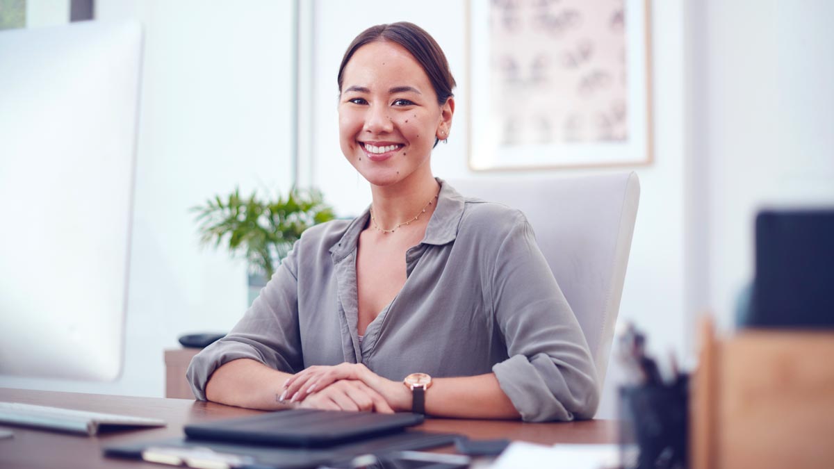 Psychotherapeutin sitzt lächelnd am Schreibtisch in moderner Praxisumgebung und arbeitet mit laptopbasierter Praxissoftware.